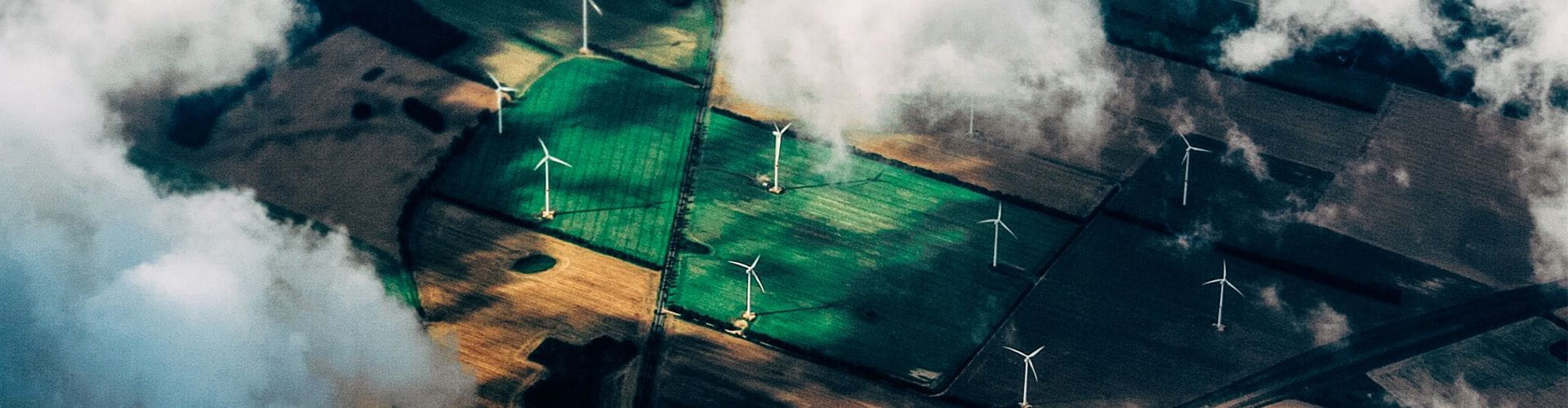 Aerial view looking through clouds down to green and brown land with wind turbines.
