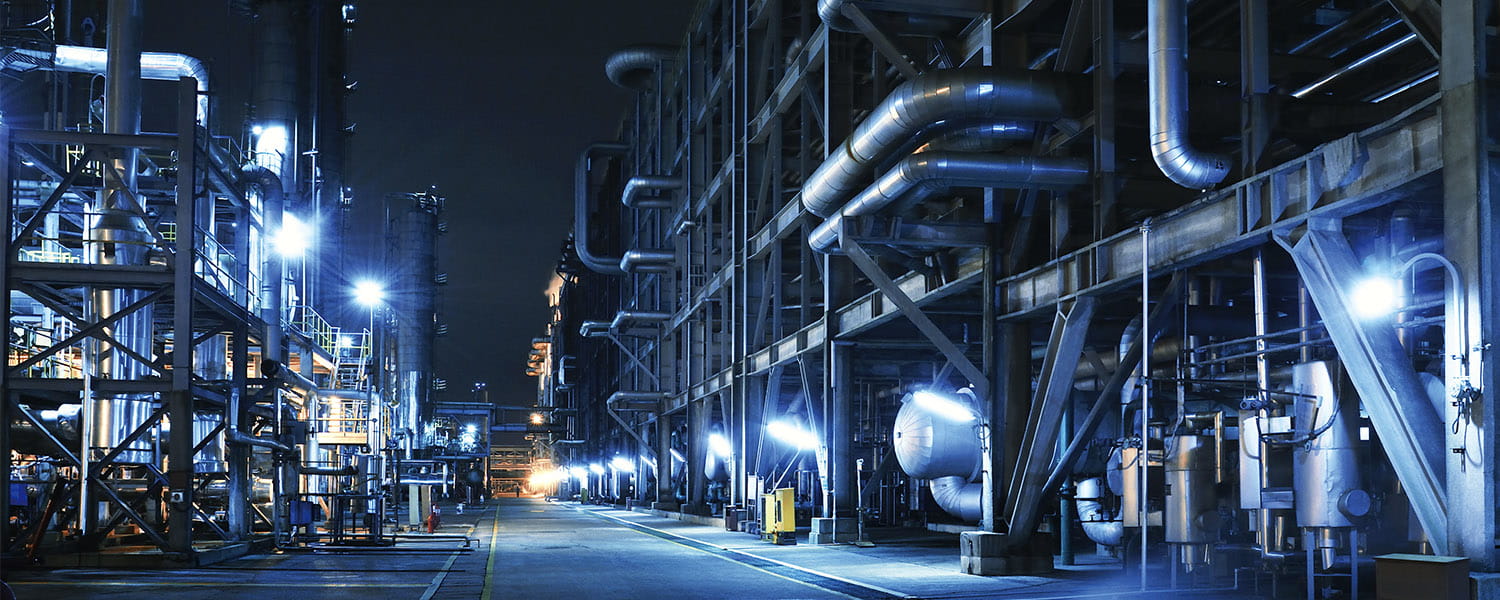 Looking down a path in between two sections of a chemical plant, at night, with several lights shining