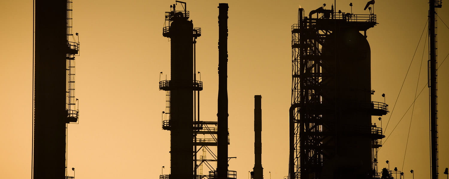 Top of towers of a refinery, with an orange sky background.