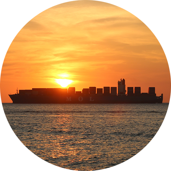 Large cargo ship in the ocean, with orange sky and sun setting.