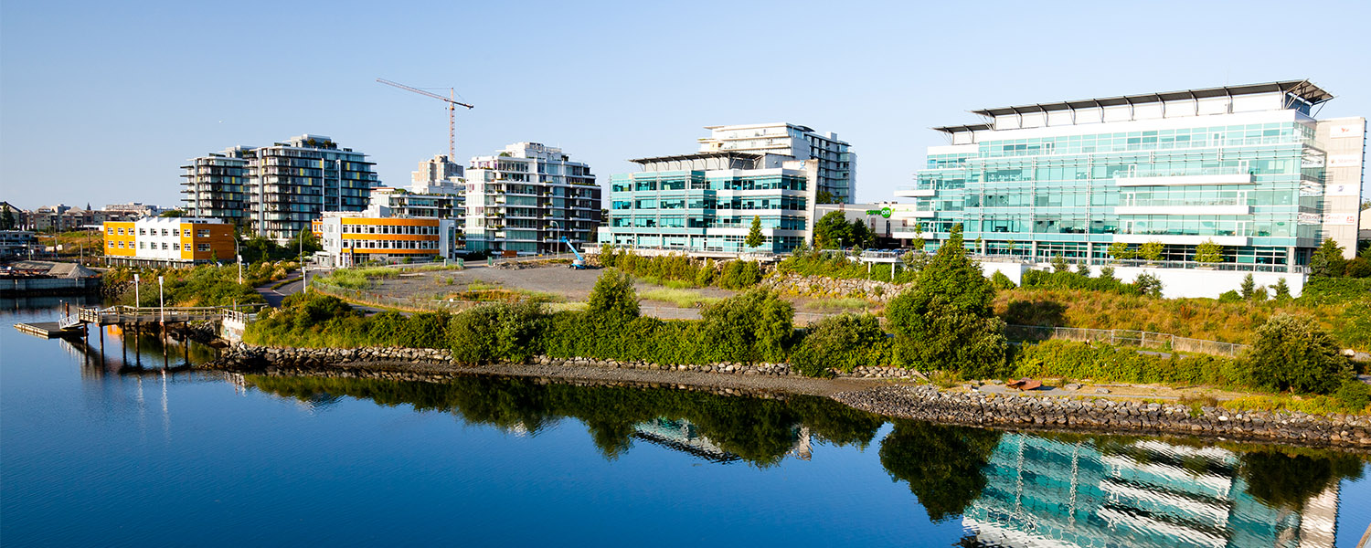 Overlooking a body of water, multiple buildings in a row, a crane in the background, reflections of the buildings in the water.